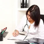 A woman in a white coat writing on a notepad, focusing on physician medical billing mistakes.